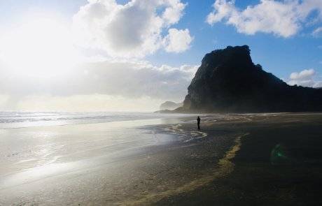 person from far away stands on beach with giant rock formation in the background